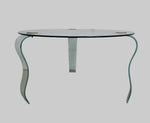 A round glass coffee table with a unique, retro-inspired design, featuring wave-like legs and minor marks.