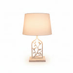 A white metal table lamp with a bird and leaf design on the base and a round shade.